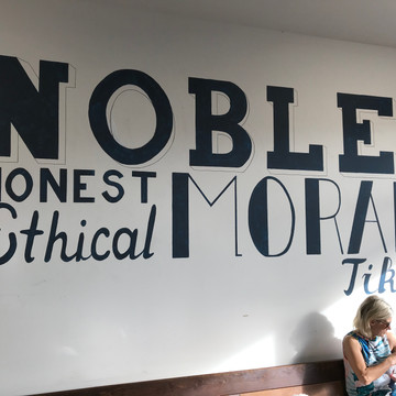 On the wall behind a patron in The Noble Merchant say noble, good, honest, ethical, moral, tika.